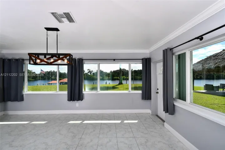 Large windows with water frontage, rectangular tile flooring, crown molding, and a metal and glass geometric chandelier