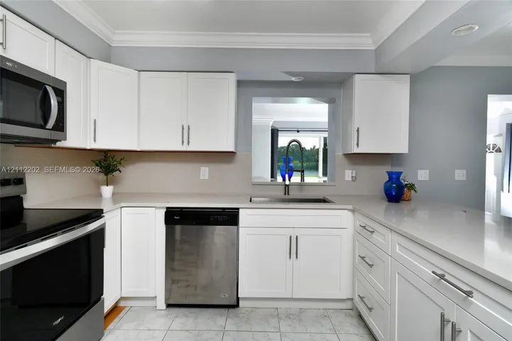 Kitchen featuring white Shaker-style cabinetry, stone-finish countertops, stainless steel appliances, a deep undermount sink with a high-arch faucet, and crown molding