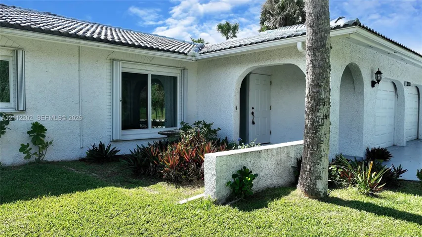 Stucco exterior featuring arched covered entryway, tile roof, and built-in wall-mounted outdoor lighting