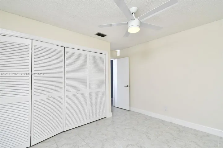 Room featuring four-panel louvered closet doors, neutral wall finish, light-toned ceramic tile flooring, and a white ceiling fan with an integrated light fixture