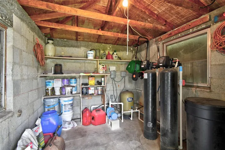 Utility space featuring exposed beam ceiling, concrete block walls, built-in open shelving, and integrated water filtration system