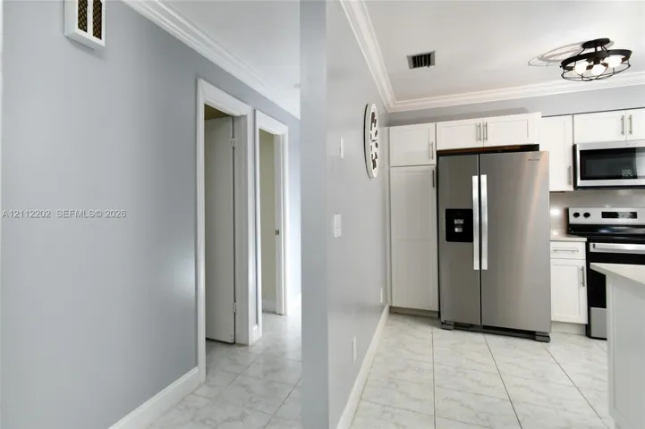 Kitchen featuring white shaker-style cabinetry, stainless steel appliances, tiled flooring, and crown molding