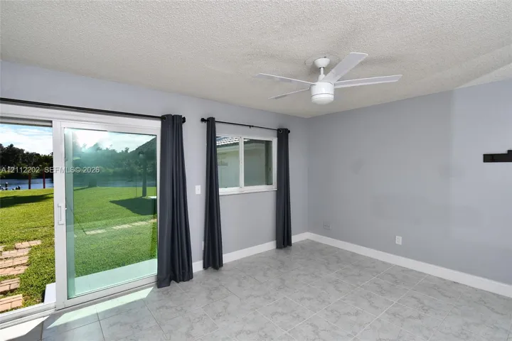 Light-toned tile flooring, white ceiling fan, and sliding glass door with exterior access to a grass lawn and waterfront scenery