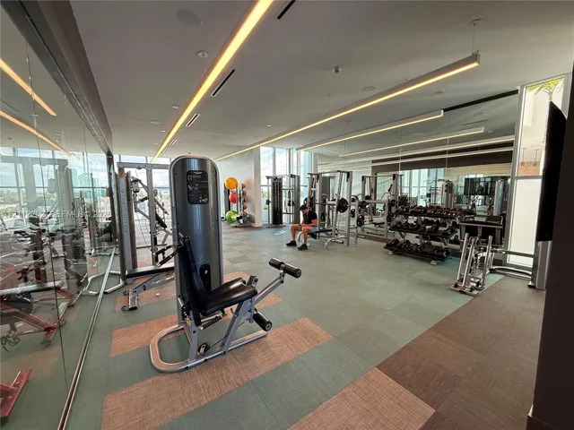 Fitness center featuring wall-to-wall mirrors, recessed linear LED lighting, floor-to-ceiling glass windows, and modular tile flooring