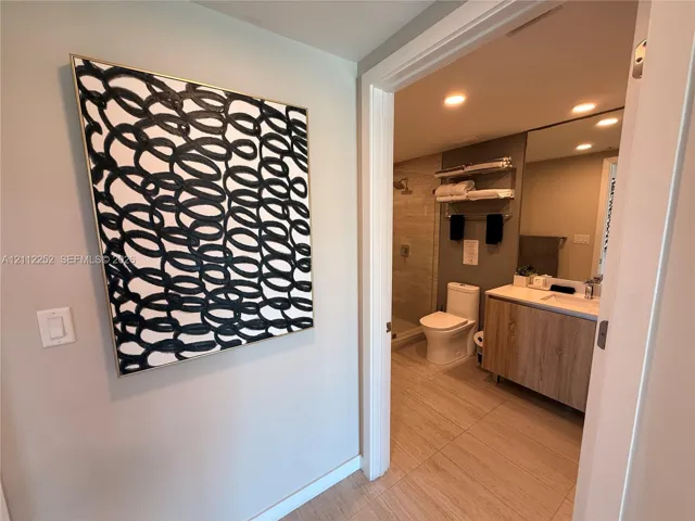Bathroom featuring a floating vanity with wood-finish cabinetry, a large wall-mounted mirror, recessed lighting, and a walk-in shower with neutral tile surround