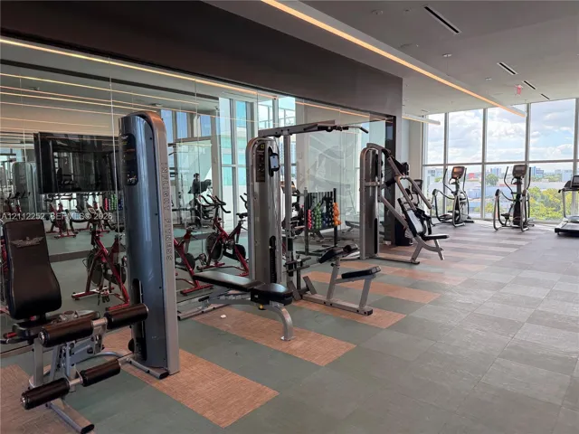 Fitness center featuring floor-to-ceiling windows, mirrored walls, recessed linear lighting, and large-format tiled flooring