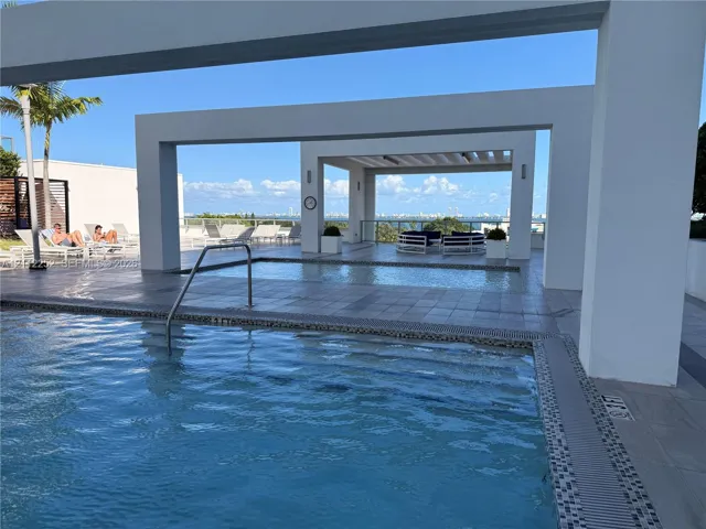 Swimming pool with metal handrail, tiled deck, and geometric overhead structures