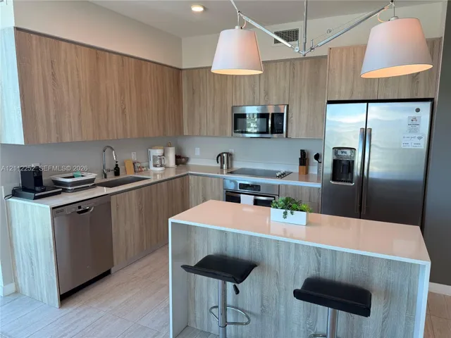 Kitchen featuring wood-finish cabinetry, white countertops, stainless steel appliances, and a waterfall-edge island with built-in seating