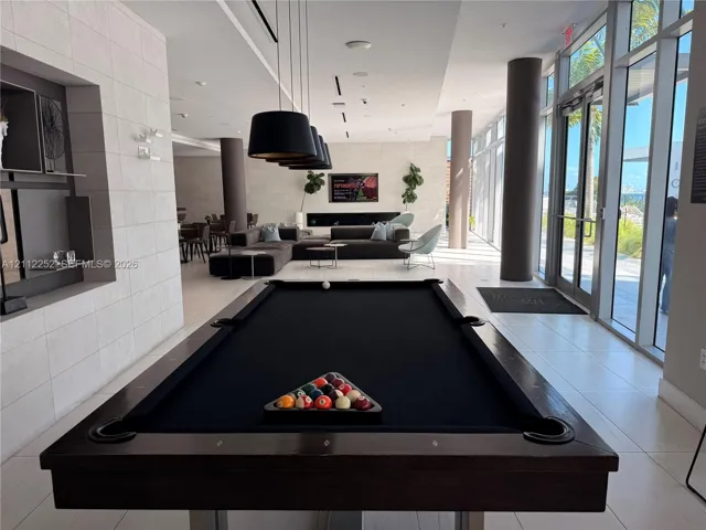 Common area featuring large-format tile flooring, floor-to-ceiling glass wall panels, built-in recessed shelving, matte black pendant lighting, and a linear fireplace