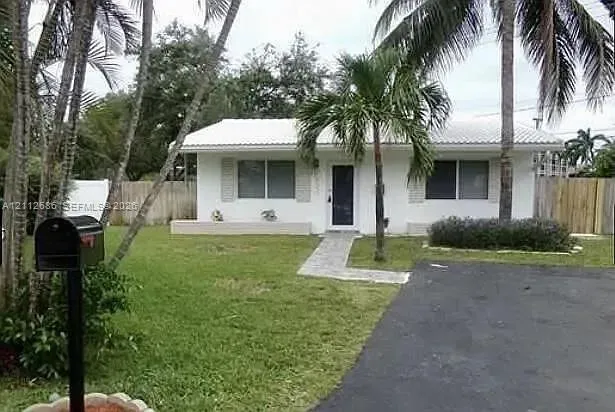 Single-story exterior featuring white stucco siding, a light-toned tile roof, a paved walkway, an asphalt driveway, and mature palm trees