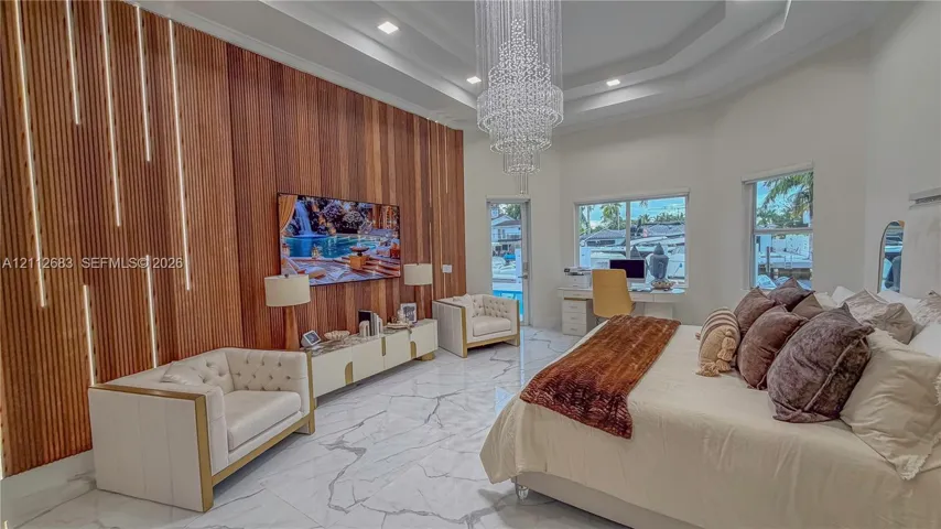 Tray ceiling with recessed lighting, large crystal chandelier, vertical wood slat accent wall with integrated LED lighting, and polished stone-finish flooring