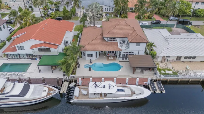 Waterfront property featuring a private boat dock, a canal-side swimming pool, a covered outdoor pavilion, and a tile roof