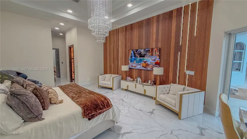 Tray ceiling with recessed lighting, large crystal chandelier, polished stone flooring, and vertical wood-slat accent wall with integrated LED strip lighting