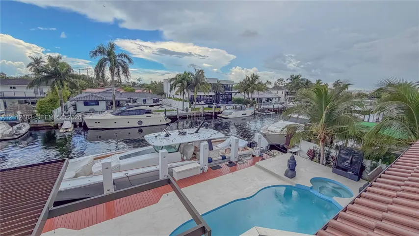 Waterfront patio featuring a custom-shaped swimming pool, integrated spa, and concrete boat dock with pilings