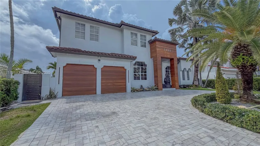 Two-story exterior featuring a stone-paver driveway, dual wood-finish garage doors, wood-paneled entryway accent, and a clay tile roof