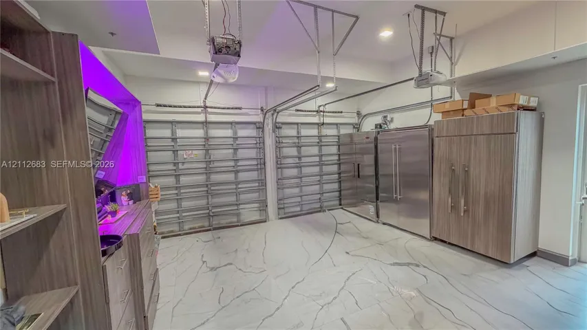 Multi-car garage featuring large-format tile flooring, integrated stainless steel refrigeration units, and custom wood-finish cabinetry