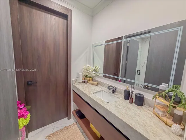 Floating vanity featuring a natural stone countertop, rectangular undermount sink, matte black faucet, and large-format wall mirror with decorative inlay