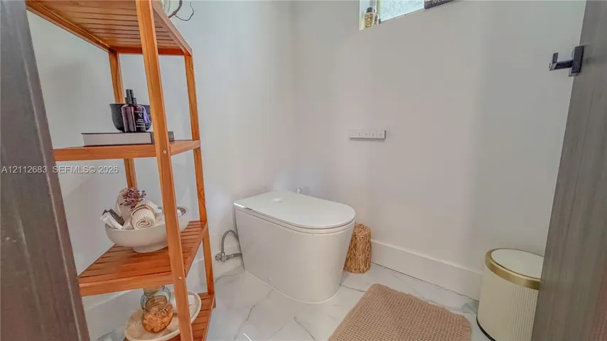 Contemporary one-piece toilet featuring a smooth, minimalist profile and high-gloss white finish, complemented by polished stone-finish flooring with distinct veining