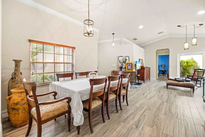 Open-concept dining area featuring vaulted ceilings, wood-finish tile flooring, crown molding, and multiple multi-light pendant fixtures