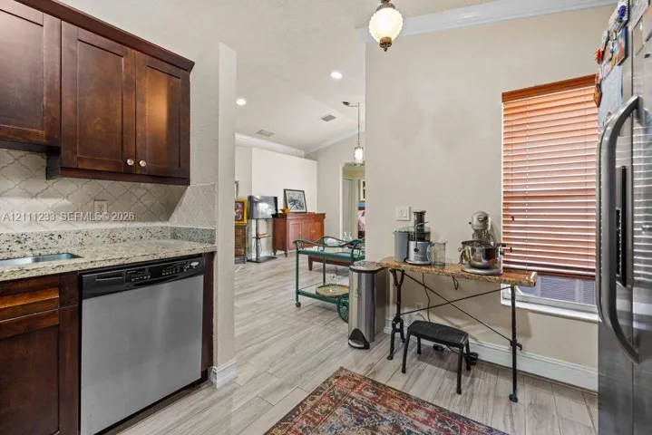 Kitchen featuring dark wood cabinetry, stone countertops, stainless steel dishwasher, arabesque tile backsplash, and wood-finish flooring