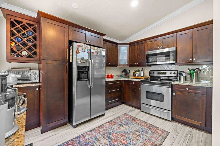 Kitchen featuring dark wood cabinetry, built-in wine rack, stone countertops, stainless steel appliances, and wood-finish tile flooring