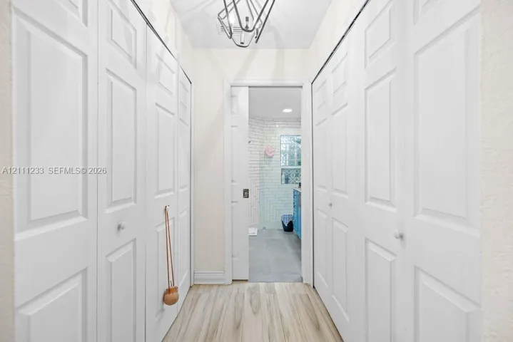 Hallway featuring wood-finish flooring, dual sets of floor-to-ceiling bi-fold closet doors, and a geometric metal pendant light fixture