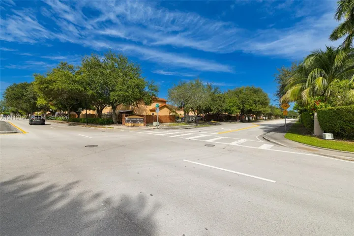 Street-level perspective featuring paved intersection, marked crosswalks, mature landscape canopy, and established green space