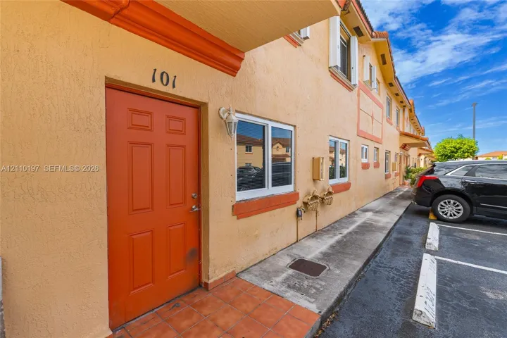 Stucco exterior featuring a bold-colored entry door, tiled porch, and multi-paned windows