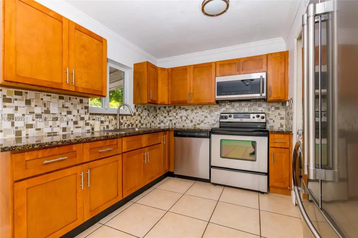Kitchen featuring shaker-style wood cabinetry, stone countertops, a mosaic tile backsplash, stainless steel appliances, and tile flooring