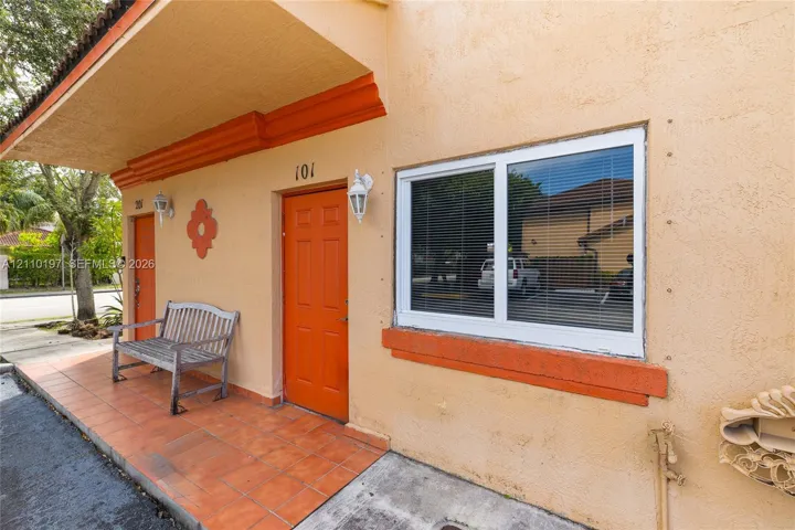 Stucco exterior featuring an extended overhang, tiled entry porch, and dual orange-finished entry doors with wall-mounted lanterns
