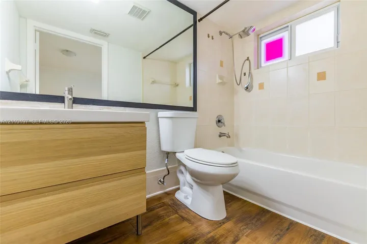 Bathroom featuring a floating vanity with wood-finish cabinetry, a large wall-mounted mirror with a dark frame, a tub-shower combination with ceramic wall tile, and wood-finish flooring