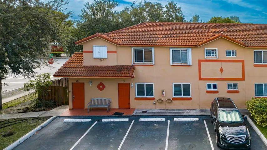 Two-story exterior featuring a clay tile roof, stucco facade, and dedicated paved parking spaces