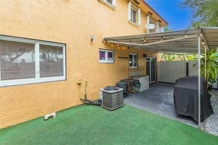 Stucco exterior featuring a covered patio, concrete flooring, exterior string lighting, and white-framed windows