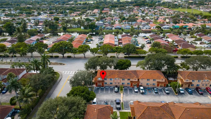 Aerial perspective of a multi-story residential building featuring a tile roof, tan stucco facade, and an integrated asphalt parking lot