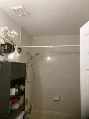 Bathtub and shower combination featuring neutral ceramic wall tile, a hand-held shower fixture, and a built-in recessed soap dish