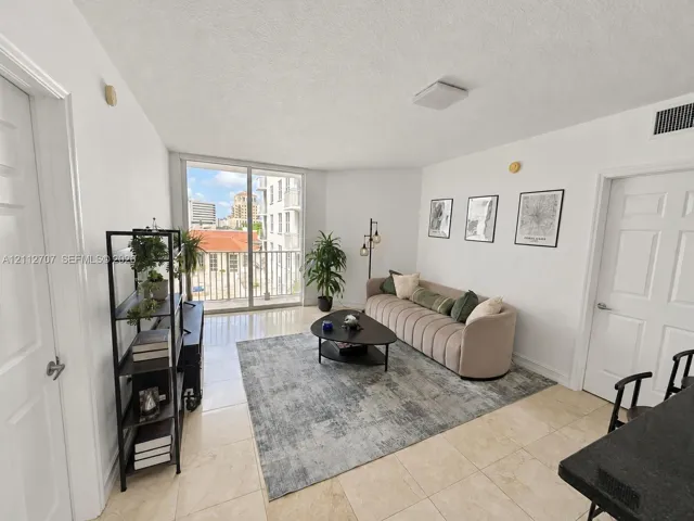 Light-filled living area featuring floor-to-ceiling glass sliding doors, neutral tile flooring, and a private balcony