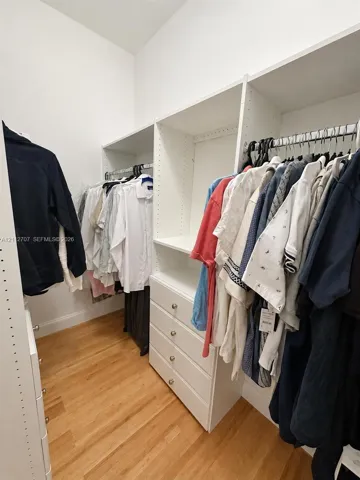 Custom closet system featuring white built-in shelving, integrated dresser drawers with chrome hardware, and multiple clothing rods finished with wood-finish flooring