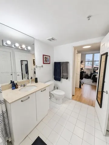 Bathroom featuring white cabinetry, integrated sink with light-toned stone countertop, full-width vanity mirror, and ceramic tile flooring
