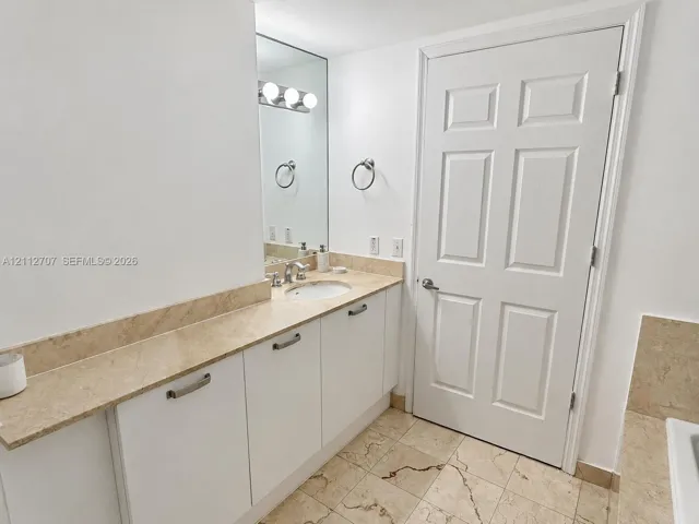 Vanity featuring stone-surfaced countertop, integrated basin, white cabinetry with metallic hardware, and wall-mounted vanity lighting