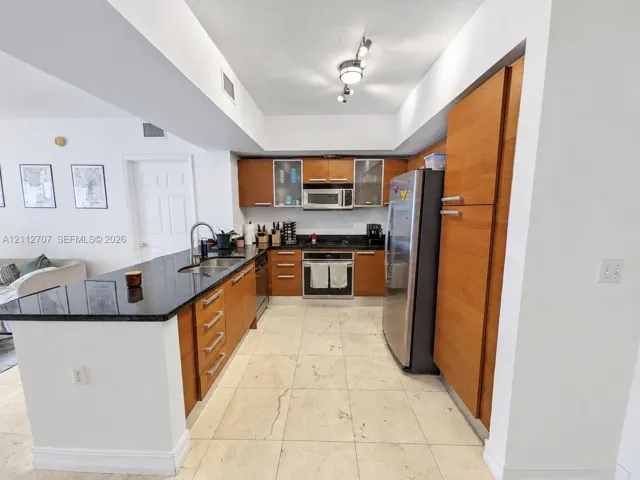 Kitchen featuring wood cabinetry, stone countertops, stainless steel appliances, tiled flooring, and track lighting