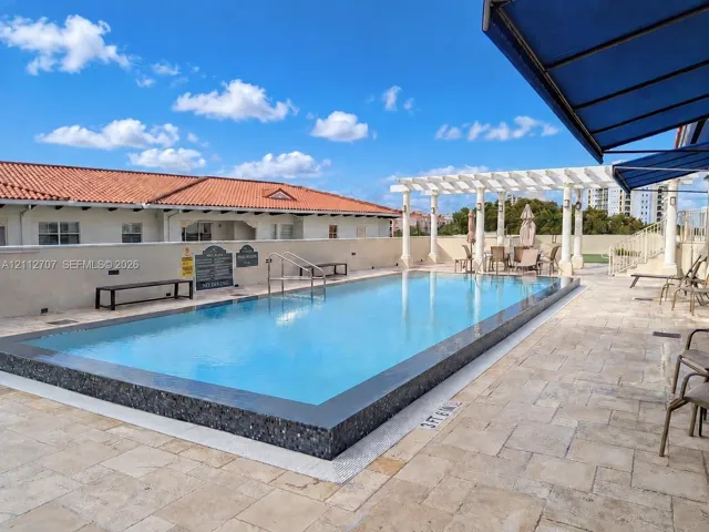 Swimming pool with tiled coping, stone-paver decking, and a white pergola structure