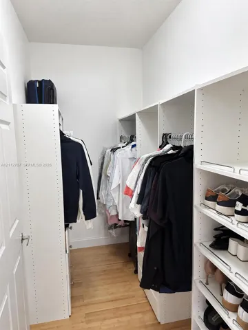 Custom walk-in closet featuring white modular shelving, multi-level hanging rods, integrated shoe storage, and wood-finish flooring