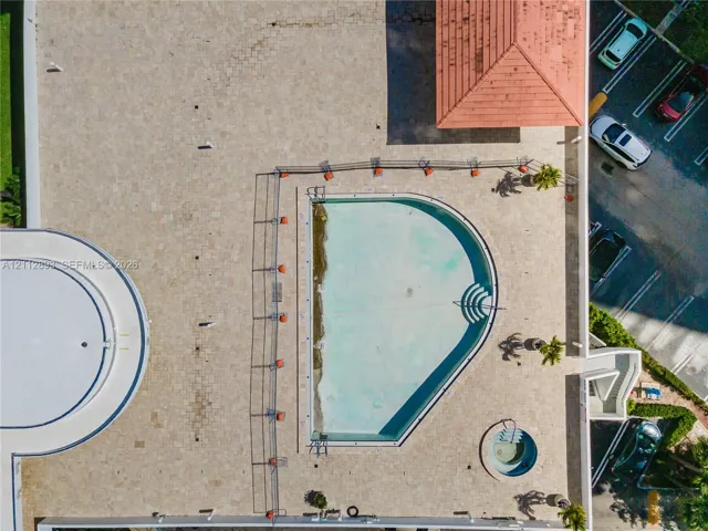 Aerial view of a sprawling pool deck featuring stone-tiled hardscaping, an in-ground swimming pool, a separate circular spa, and a covered pavilion structure