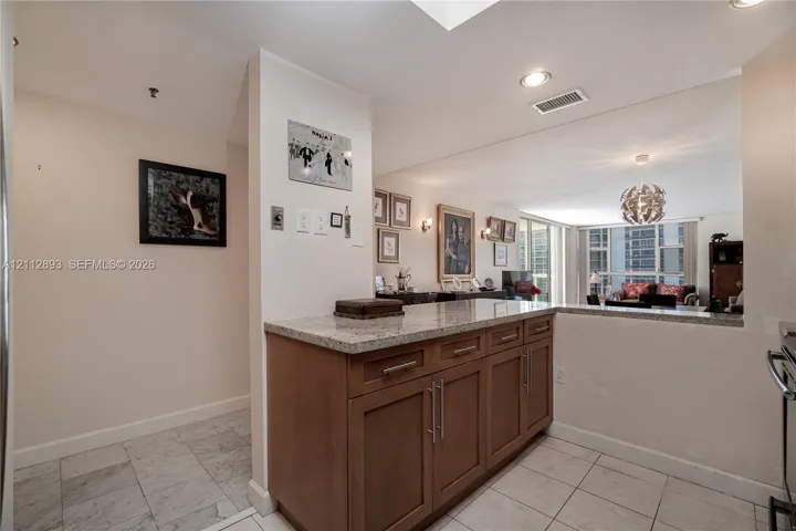 Kitchen area featuring wooden cabinetry with stainless steel bar pulls, stone-composite countertops, recessed lighting, and tile flooring