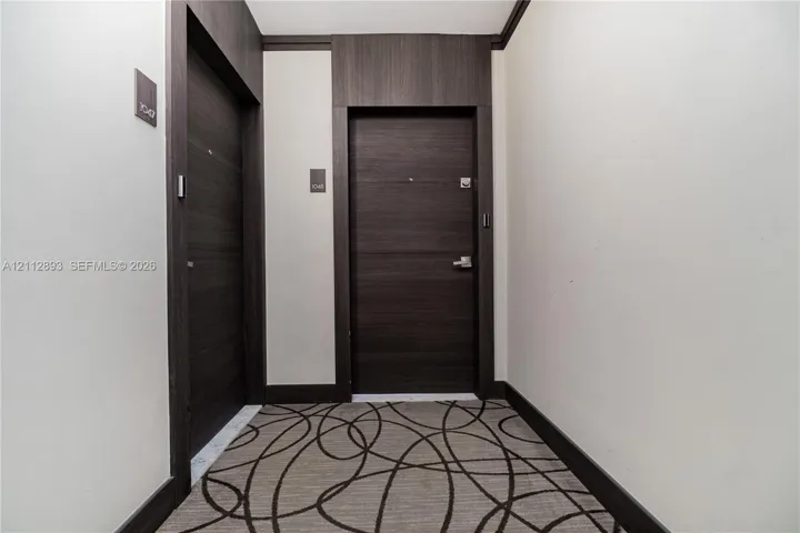 Entryway featuring two dark wood-finish doors with brushed metal hardware, high-contrast dark wood-finish door casing and trim, and patterned wall-to-wall carpeting