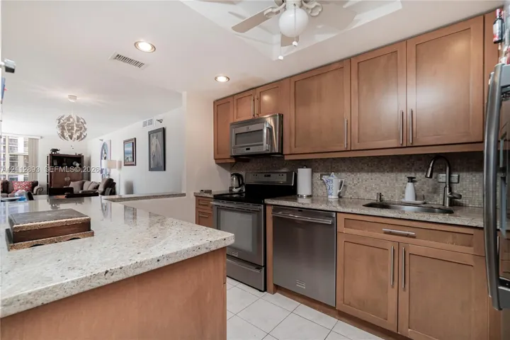 Kitchen featuring wood cabinetry, stone countertops, stainless steel appliances, tiled backsplash, and recessed lighting