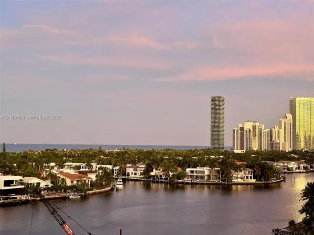 Waterfront landscape featuring a winding canal, mature palms, residential structures, and a distant coastal horizon