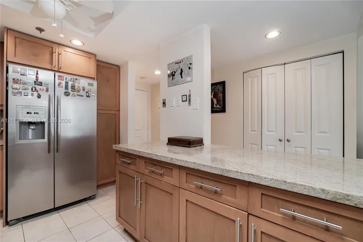 Kitchen featuring wood cabinetry, stone-finish countertops, stainless steel refrigerator, recessed lighting, and white bifold closet doors