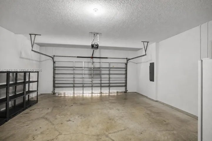 Enclosed garage featuring a concrete floor, automated door system, ceiling-mounted opener, and white walls