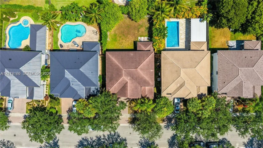Aerial perspective of residential properties featuring hip-style roofing, paved driveways, and mature landscaping